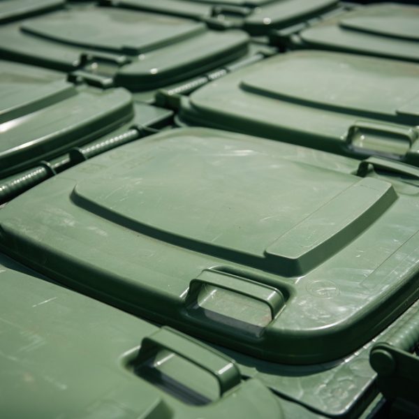 Daudzi zaļi plastmasas atkritumu konteineru vāki izvietoti rindās, redzami tuvplānā.