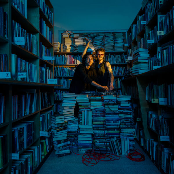 Divi smaidīgi vīrieši, viens ar tumšām saulesbrillēm un tetovētām rokām, blāvi apgaismotā bibliotēkā veido mūziku pie dīdžeja aprīkojuma "Pioneer DJ", kas novietots uz augstas grāmatu kaudzes. Viņu apkārtnē ir plaukti pilni ar grāmatām un grīda ir nokrauta ar papildu grāmatu kaudzēm.